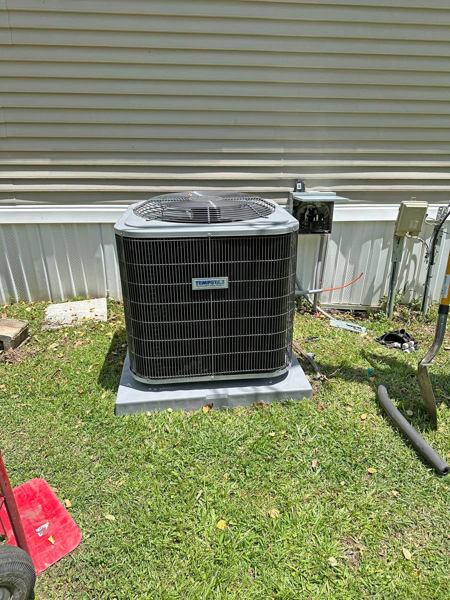 New condenser set on a fresh pad beside a mobile home