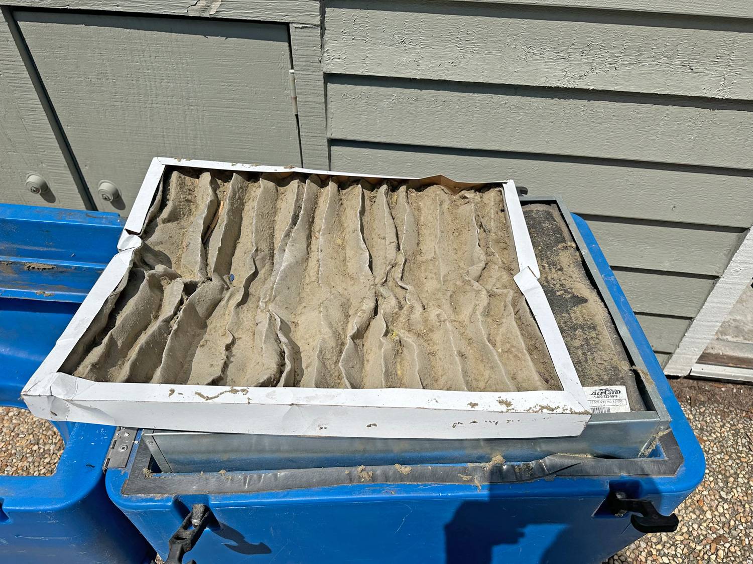 Badly clogged air filter pulled from a system, laid on a blue bin