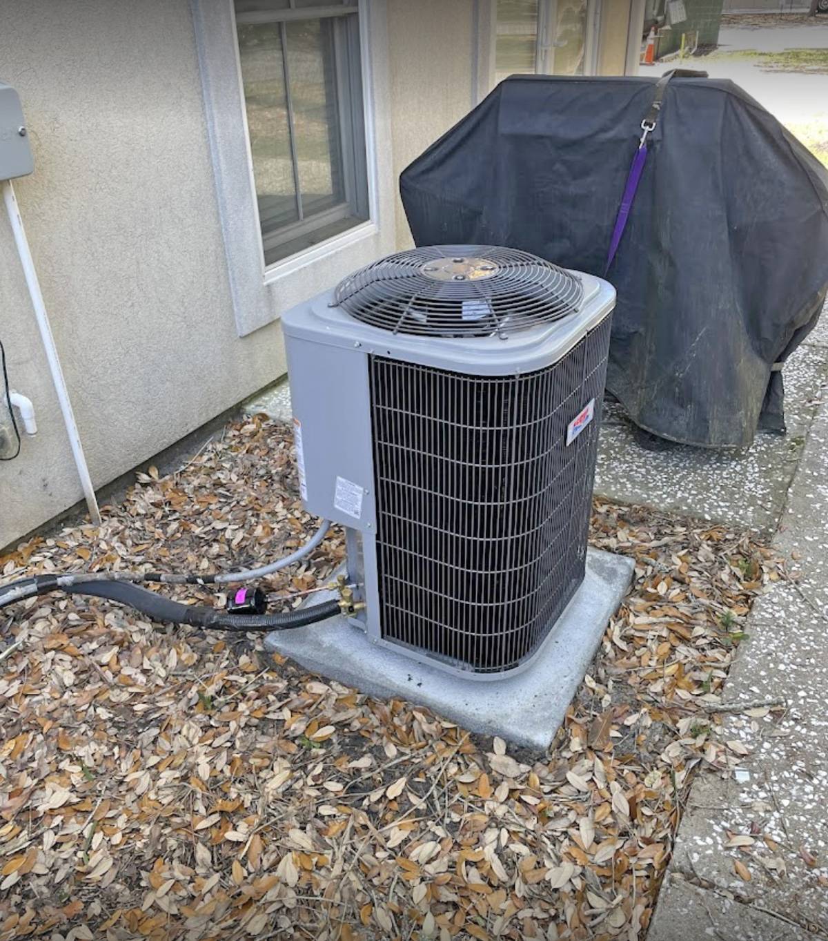 New condenser installed beside a house, leaves on the ground