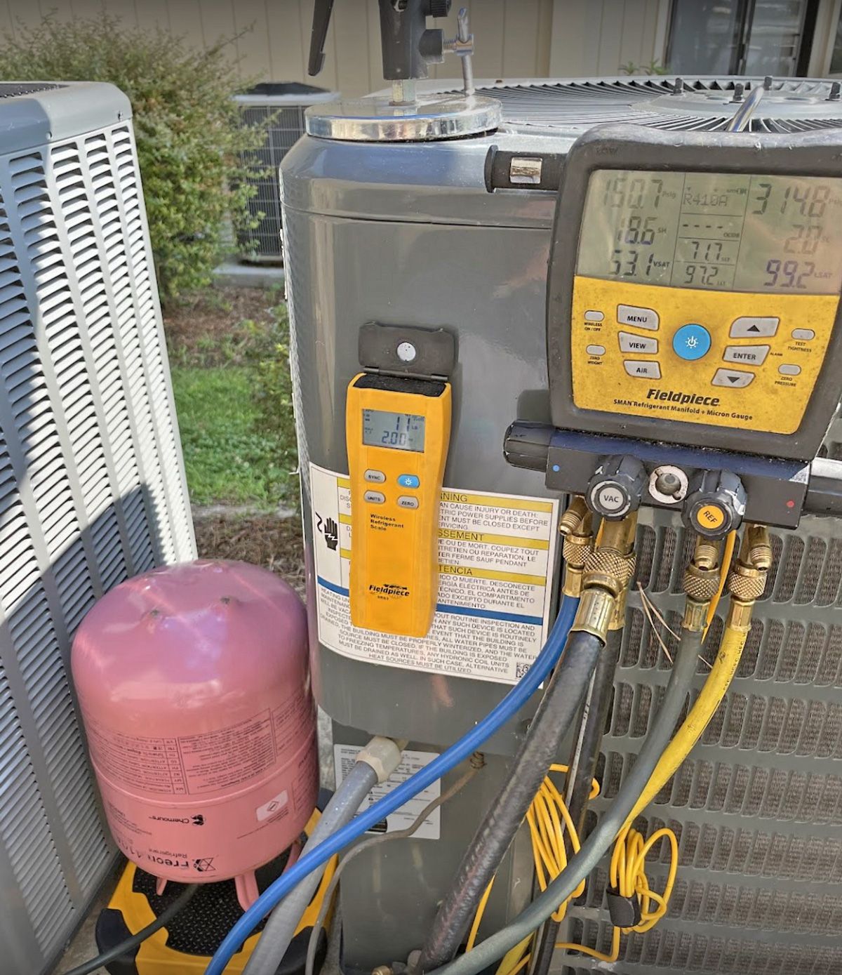 Fieldpiece digital gauges and refrigerant tank hooked to a condenser during a charge check