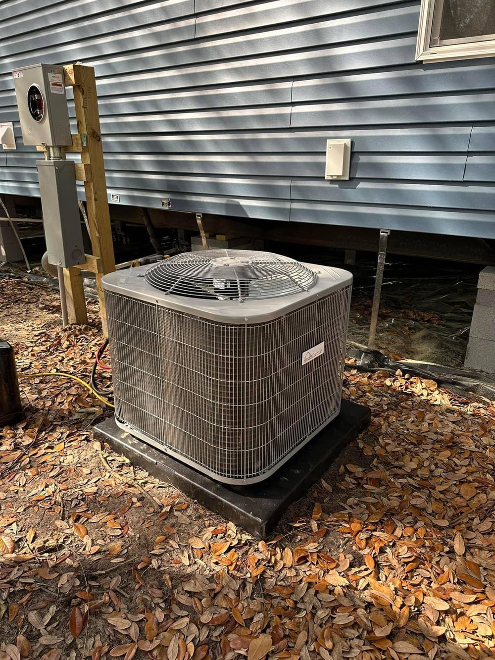 New condenser on a black pad beside a raised mobile home