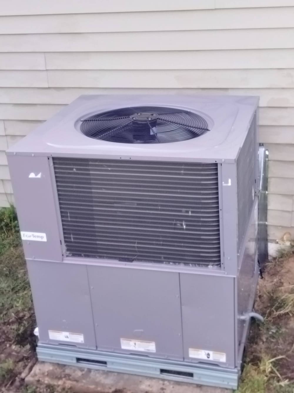 Gray package unit on a pad beside a house